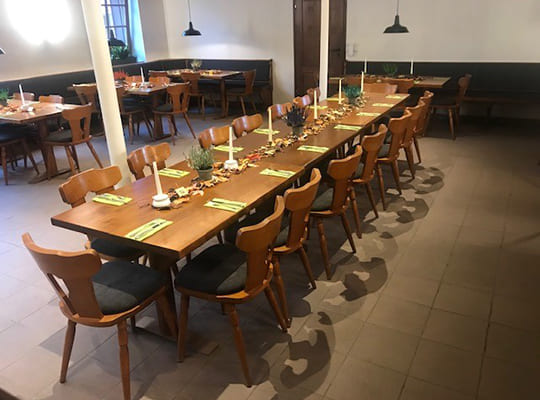 Mitten im Speisesaal steht eine lange Tischtafel angerichtet für das Dinnerkrimi Endingen am Kaiserstuhl, außen rum weitere gemütliche Sitzbänke