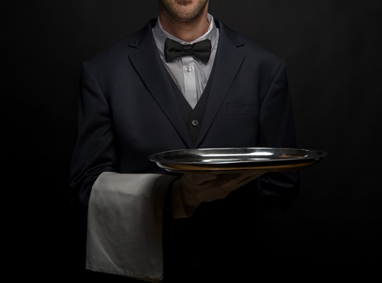Ein Kellner in schwarzem Sakko mit einem Serviertablet in der Hand